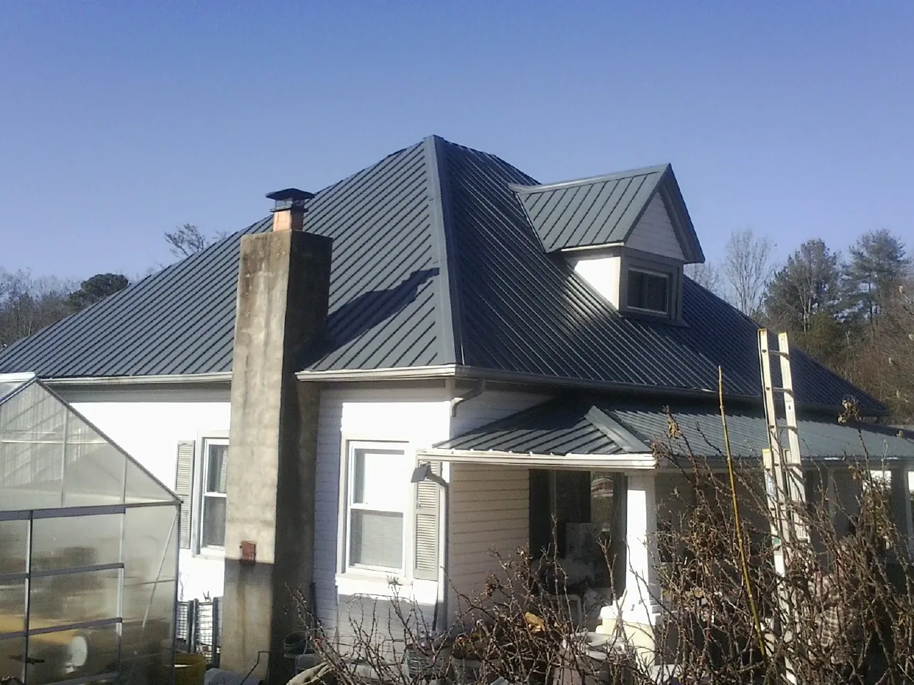 Dark blue standing seam metal roof on a white farmhouse with dormer — Slate & Tile Roof Repair by Roofing Brothers in Stacy