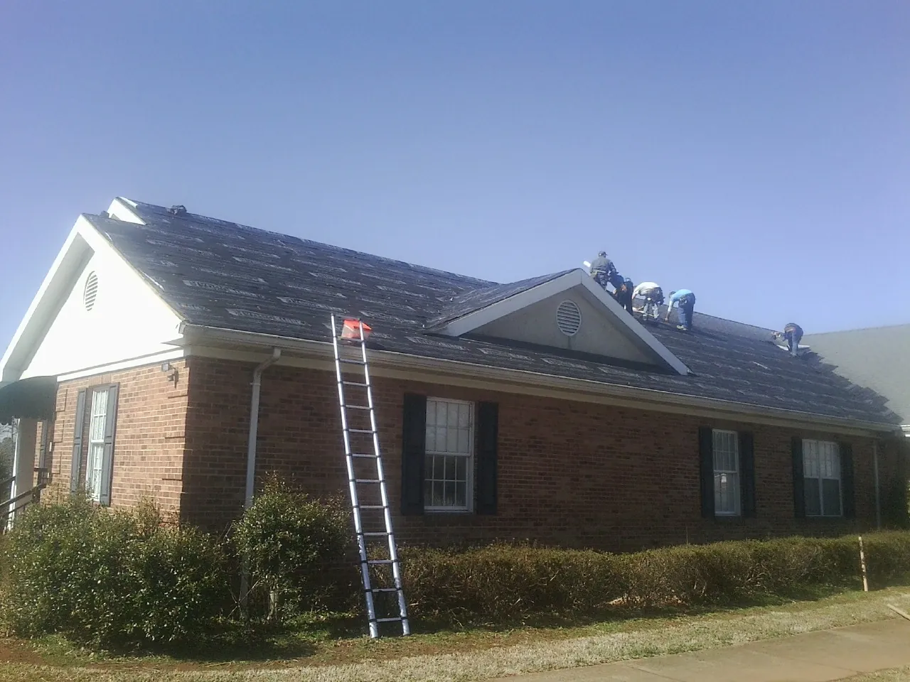 Crew tearing shingles off a brick ranch roof with a ladder set — Emergency Roof Repair work by our crew in Stacy