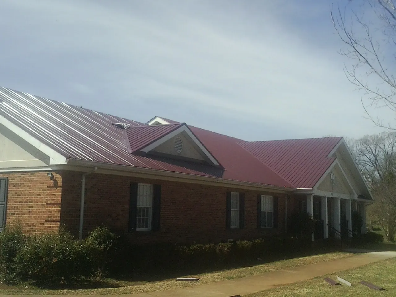 Red metal roof with gabled entries on a long brick building, from a Hail Damage Roof Repair job in Stacy