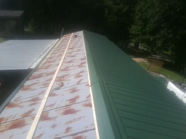 Old rusted panels beside newly installed green metal roofing — Wind Damage Roof Repair by Roofing Brothers in Stacy